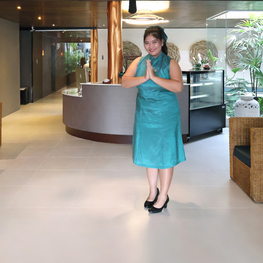 a customer service staff is welcoming a customer to Amla Aqua - Organic spa & hydrotherapy in Cherngtalay, Phuket with a warm smile and she is wearing a teal coloured skirt
